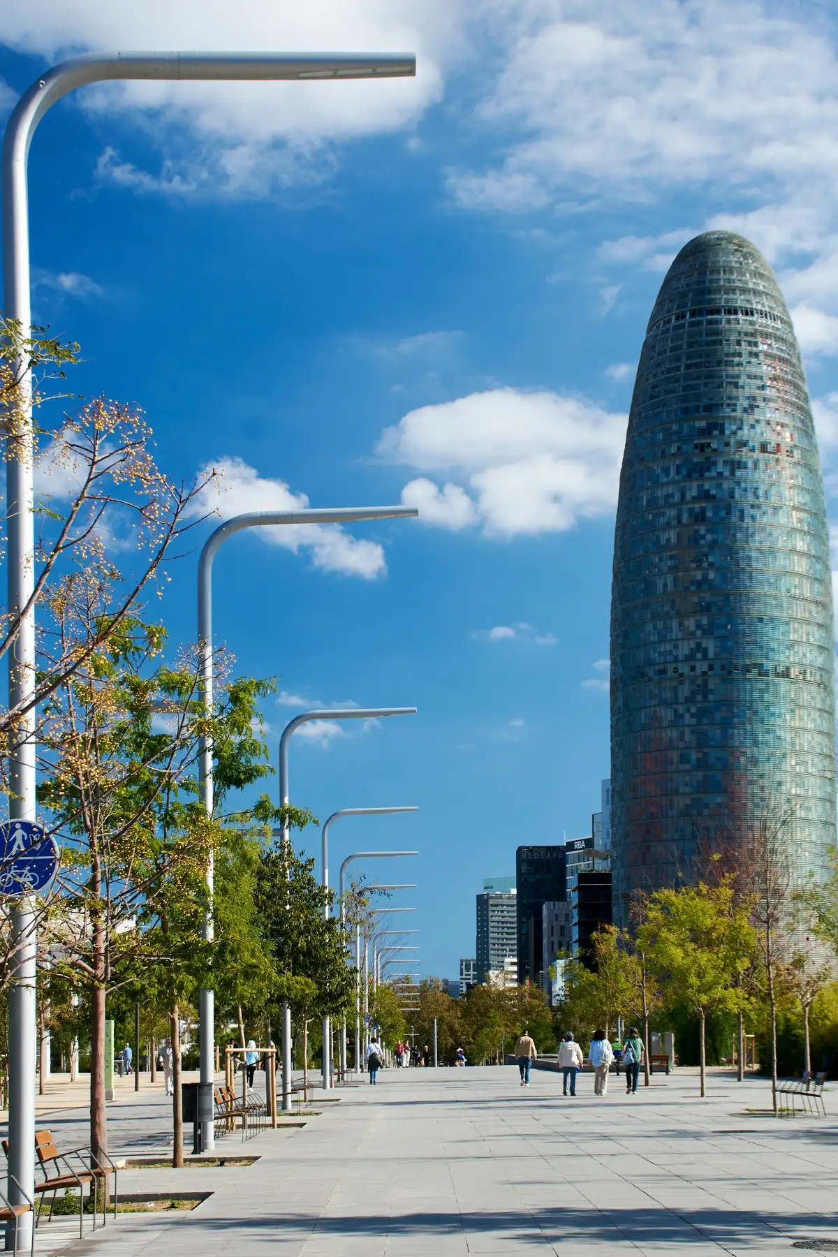 Torre Glòries rising above a tree-lined promenade in Barcelona