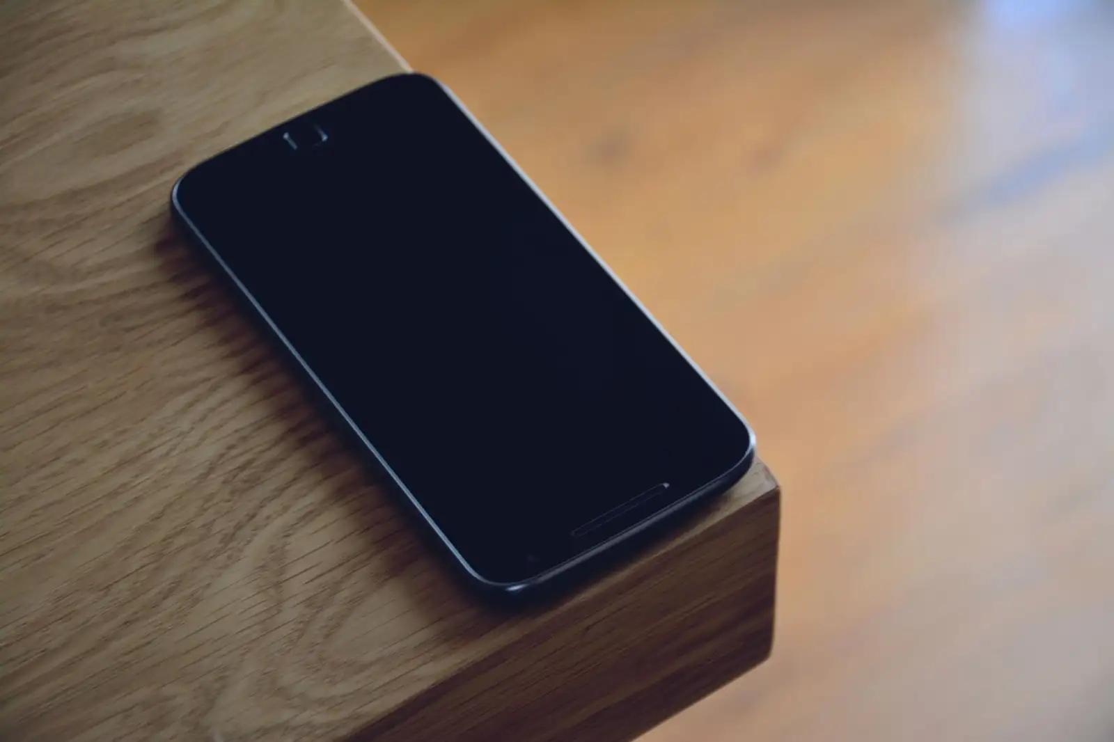 Smartphone mit dunklem Bildschirm auf der Ecke eines Holztischs