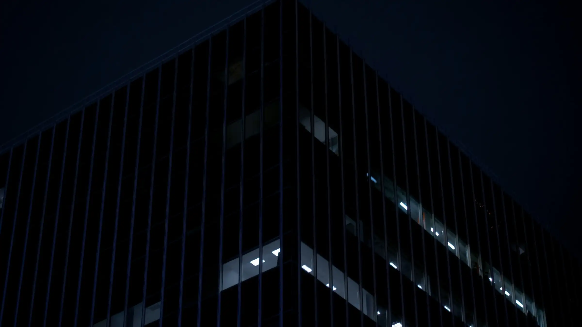 Dunkles Bürogebäude aus Glas in der Abenddämmerung mit einigen beleuchteten Fenstern