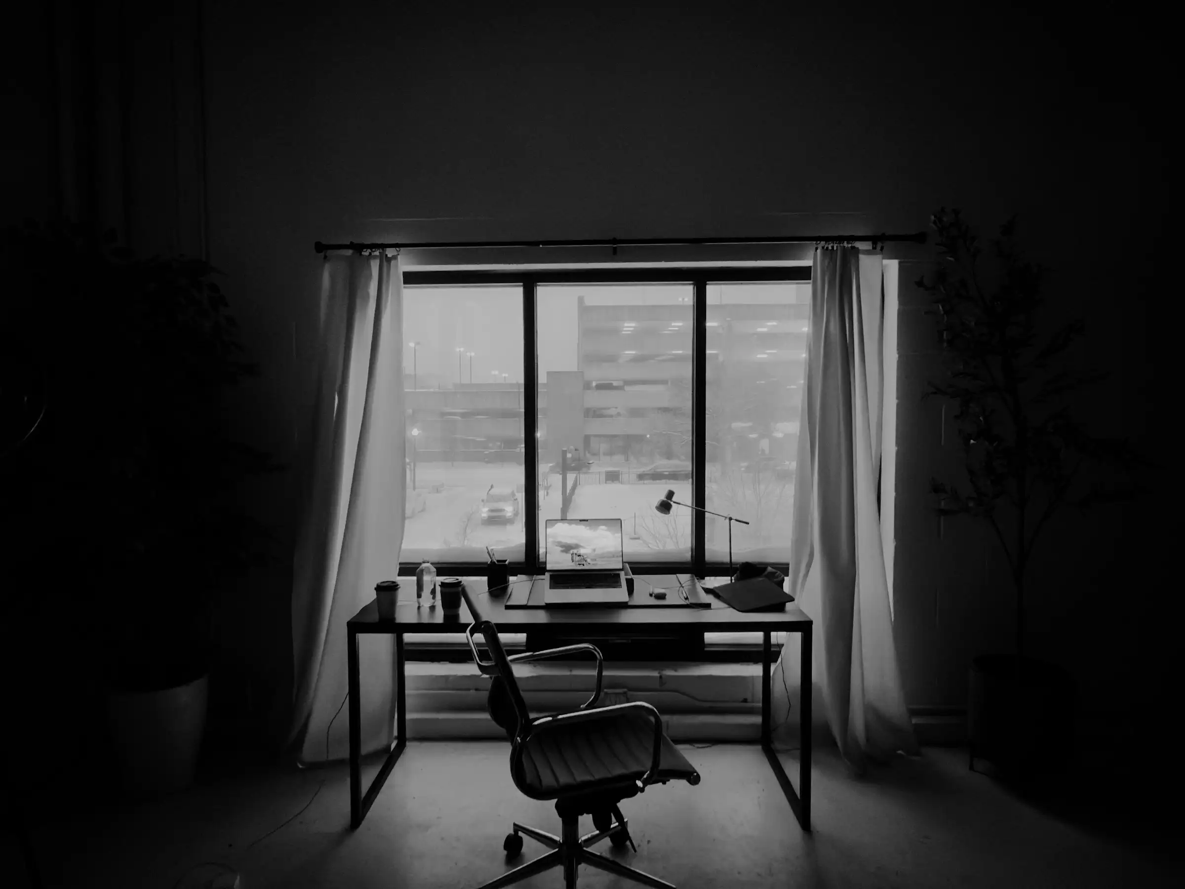 Leerer Schreibtisch mit Bürostuhl vor einem Fenster in einem dämmrigen Raum